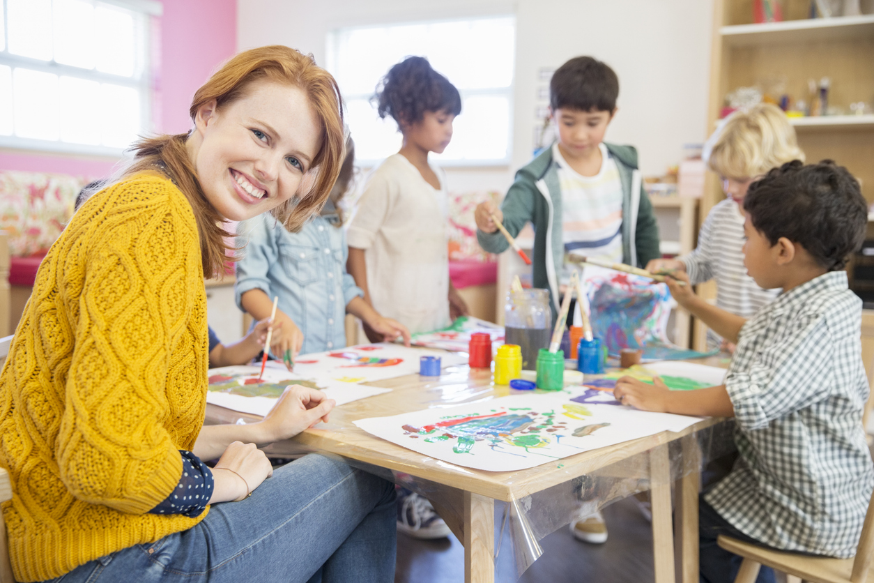 A teacher sitting with students at a table doing activities